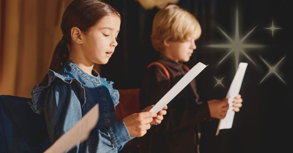 Two children reading from scripts on a stage. Use reader's theater with Tinker Book Club to increase fluency and confidence.