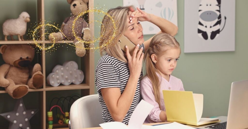 An overwhelmed homeschooling mom sits at a desk with her child on her lap. She is on the phone with her hand to her head.
