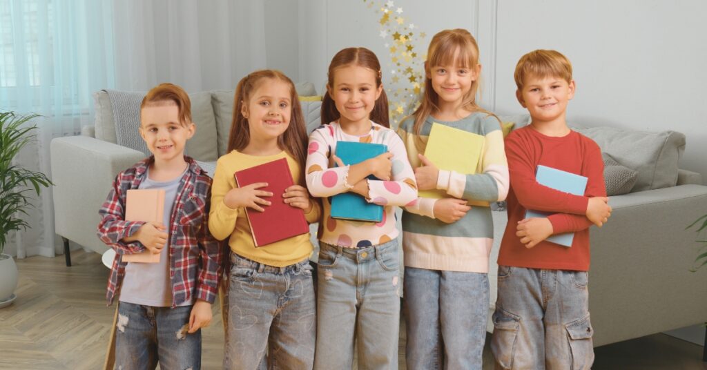 Children standing in a row, smiling, and holding books in a family room. Kids book club.